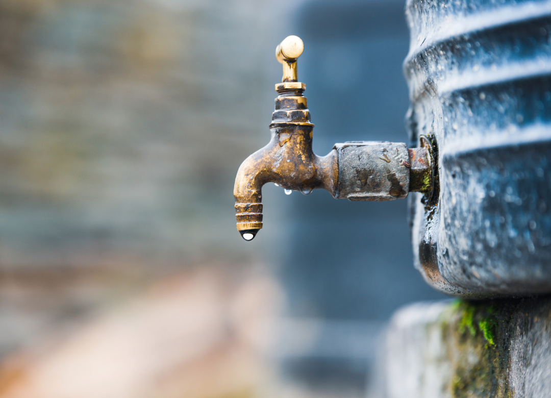 A weathered brass faucet on a concrete structure with a single water droplet.