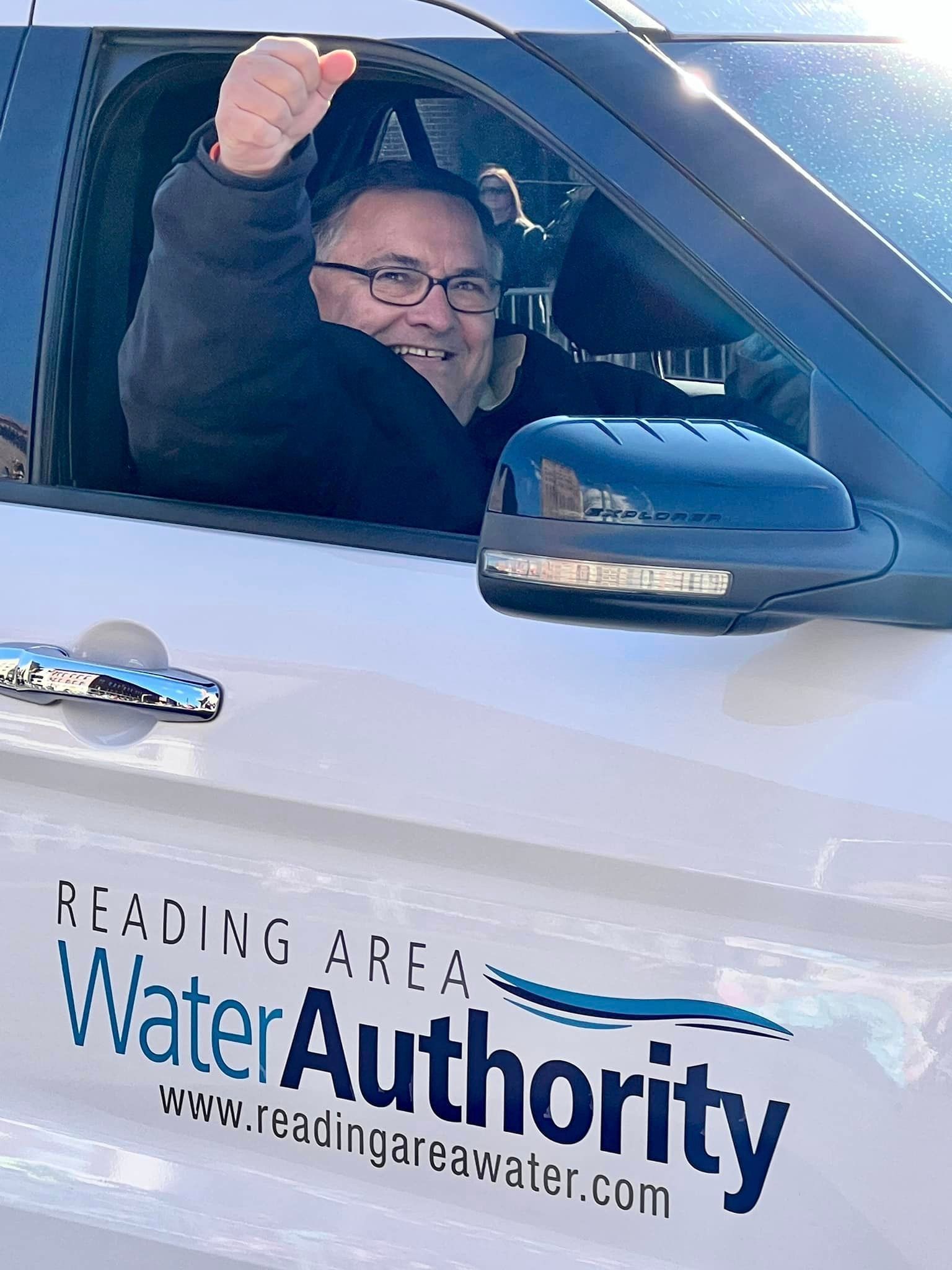 Man in Reading Area Water Authority car waving, smiling. Sunny day.