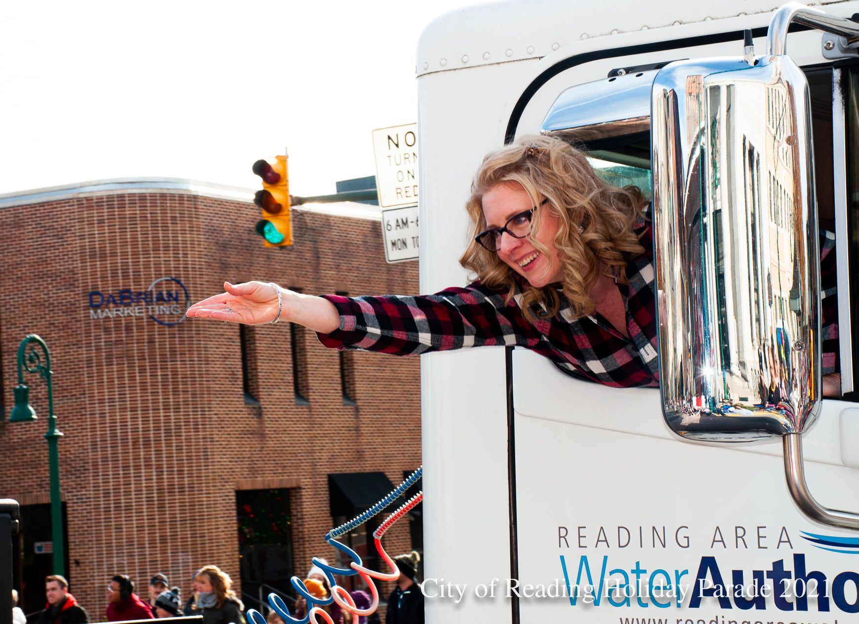 Woman in plaid leans out of a Reading Area Water Authority truck, waving.