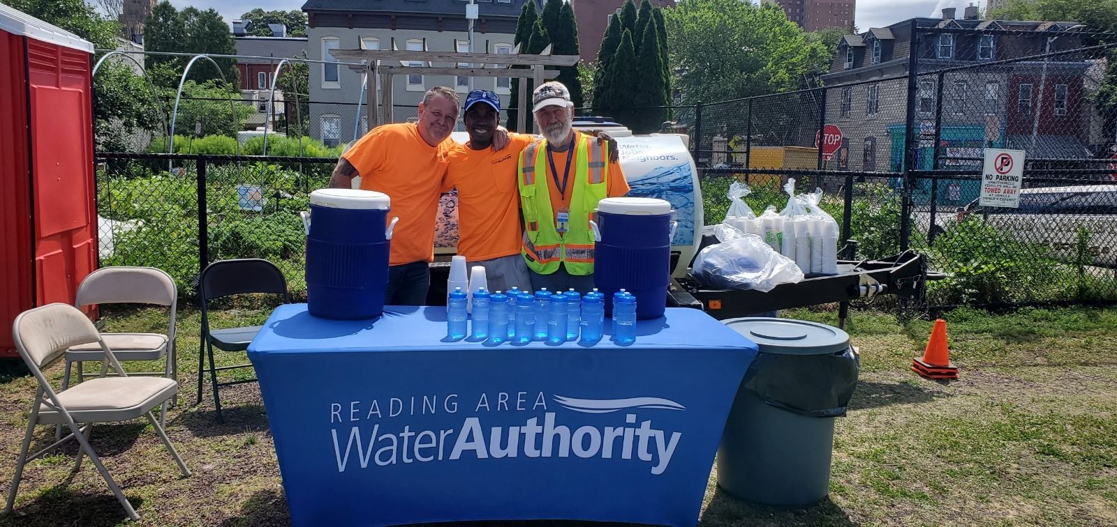Three people at a water station for the Water Authority, blue table, water bottles, and coolers.