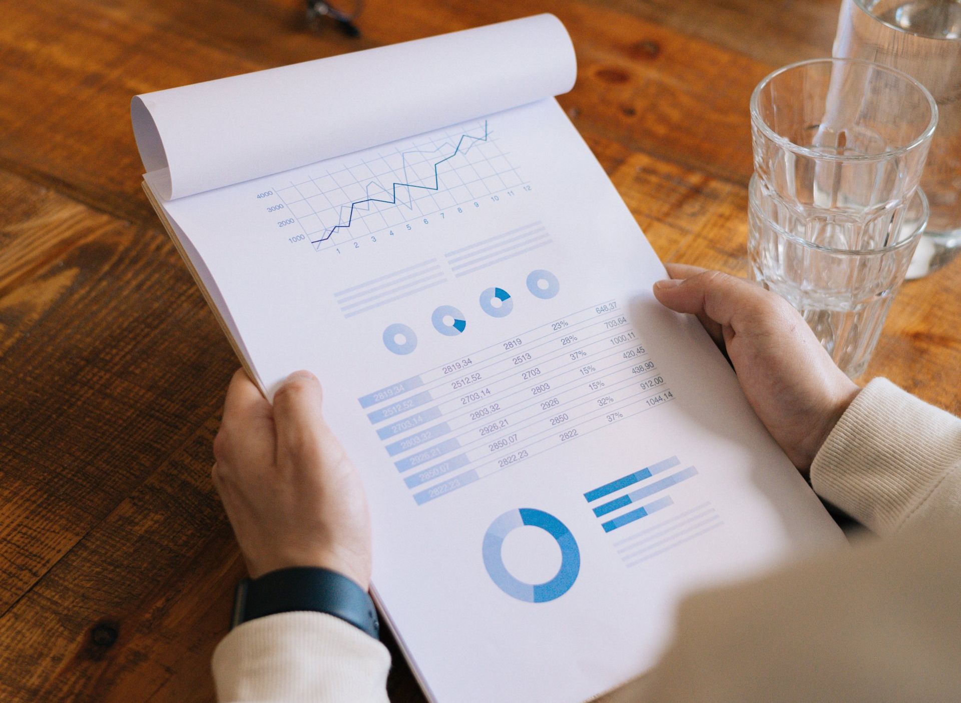 Hands holding a clipboard with business charts and graphs, on a wooden table.