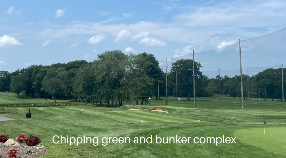 A golf course with a green and bunker complex in the background.