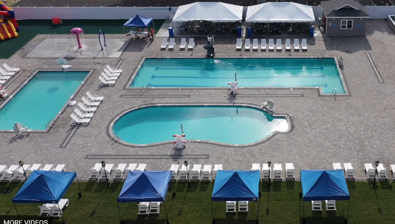 An aerial view of a swimming pool with blue tents and chairs