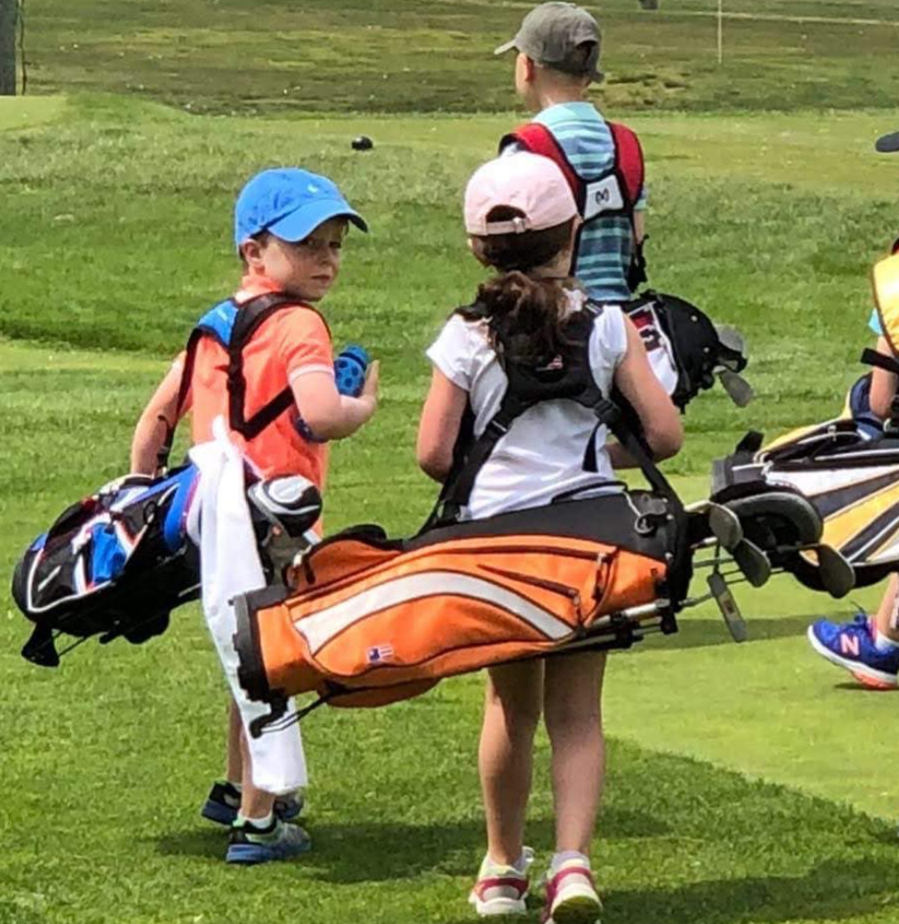 A group of children carrying golf bags on a golf course