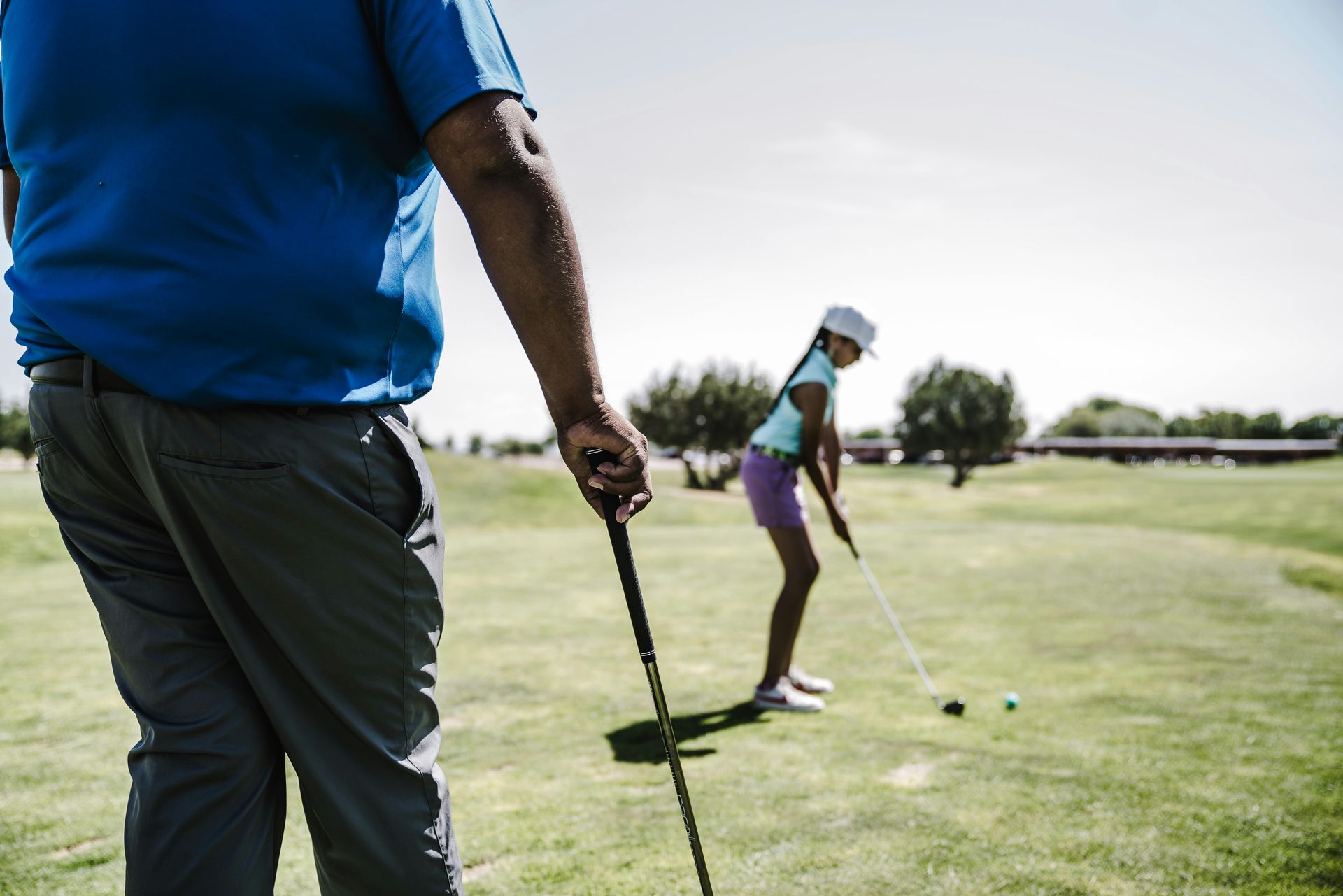 A man and a girl are playing golf on a golf course.