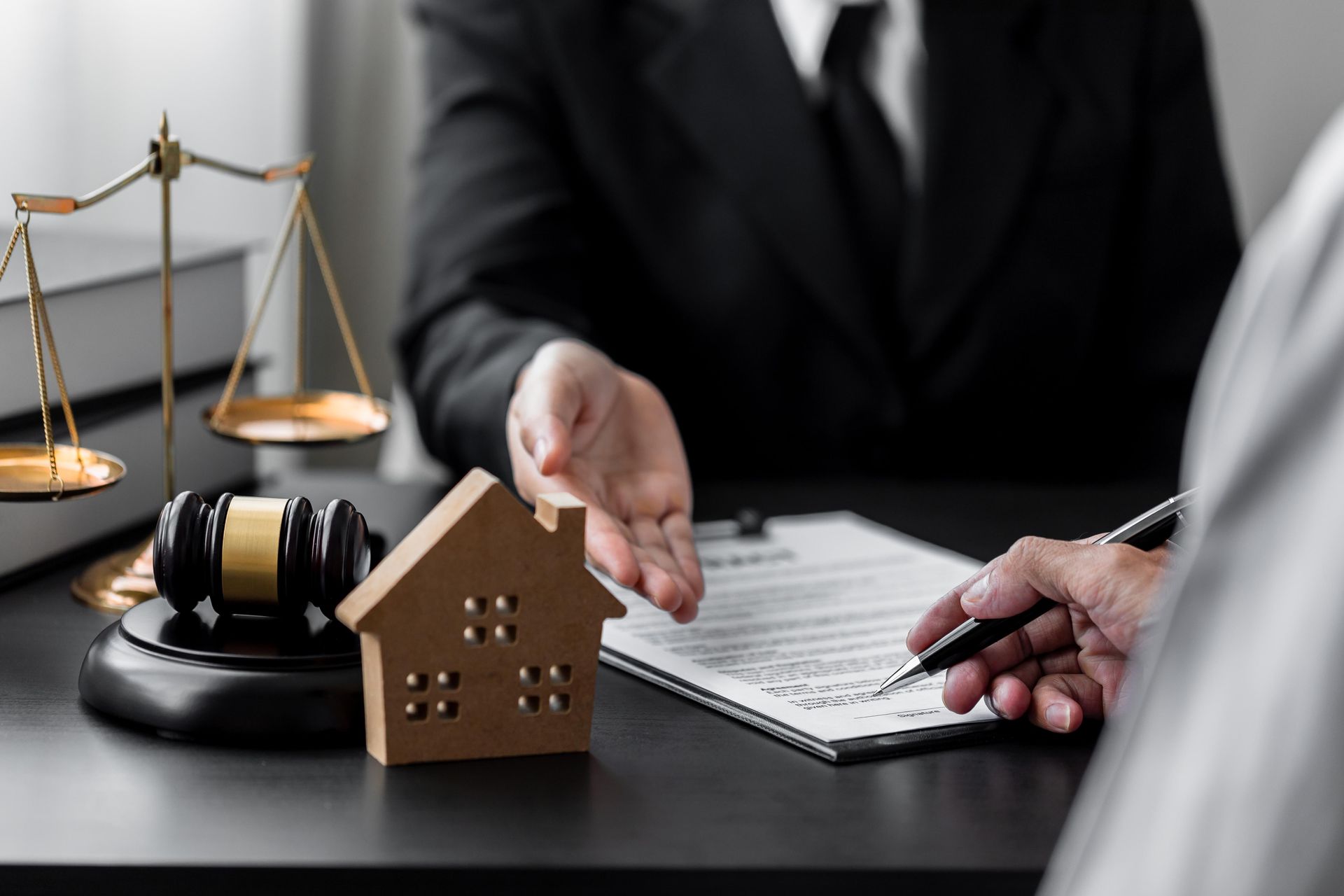 Lawyer discusses property documents beside scales, gavel, and house model at a desk