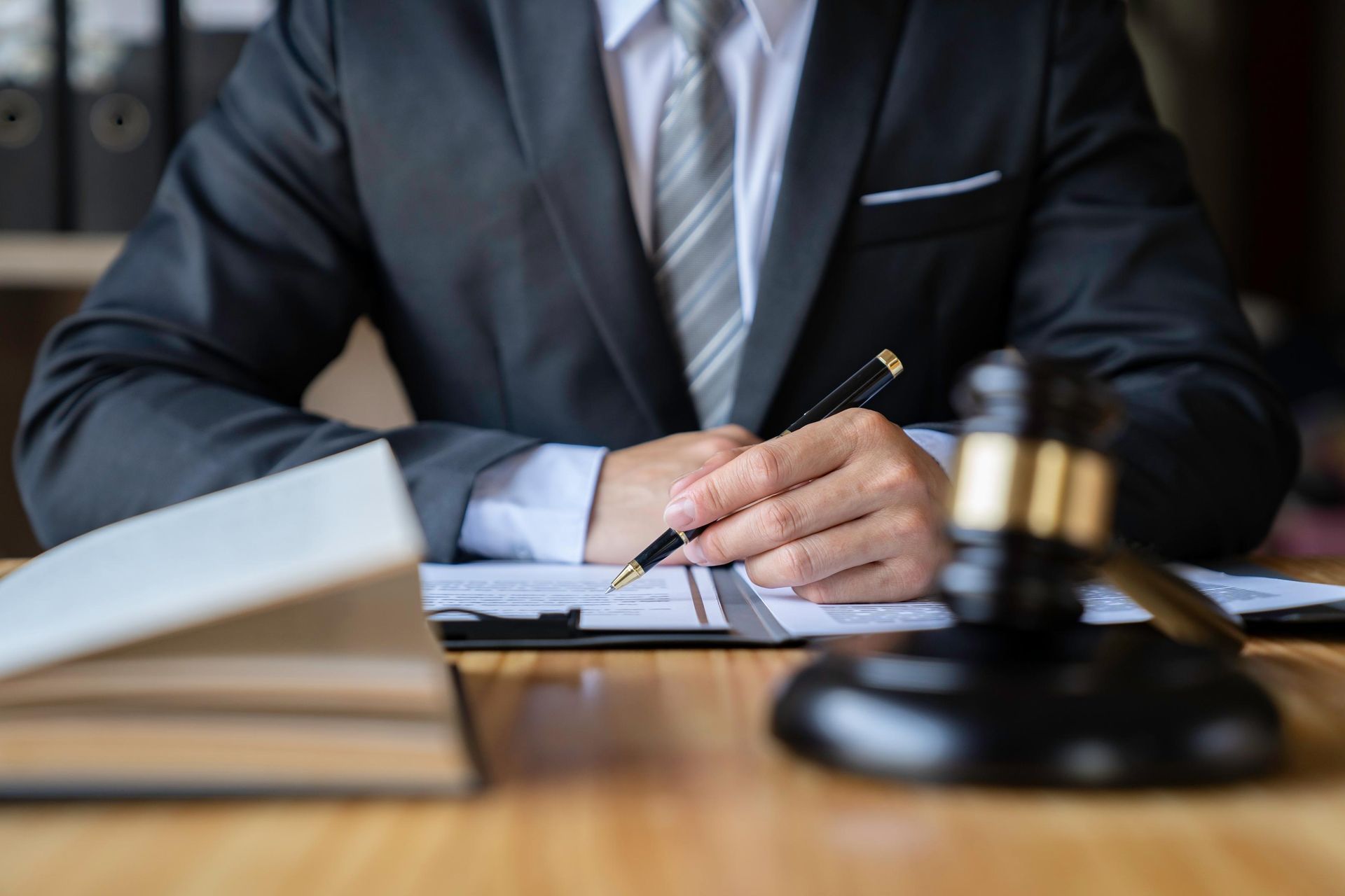 Lawyer in a suit signing documents beside a gavel and open book at a desk