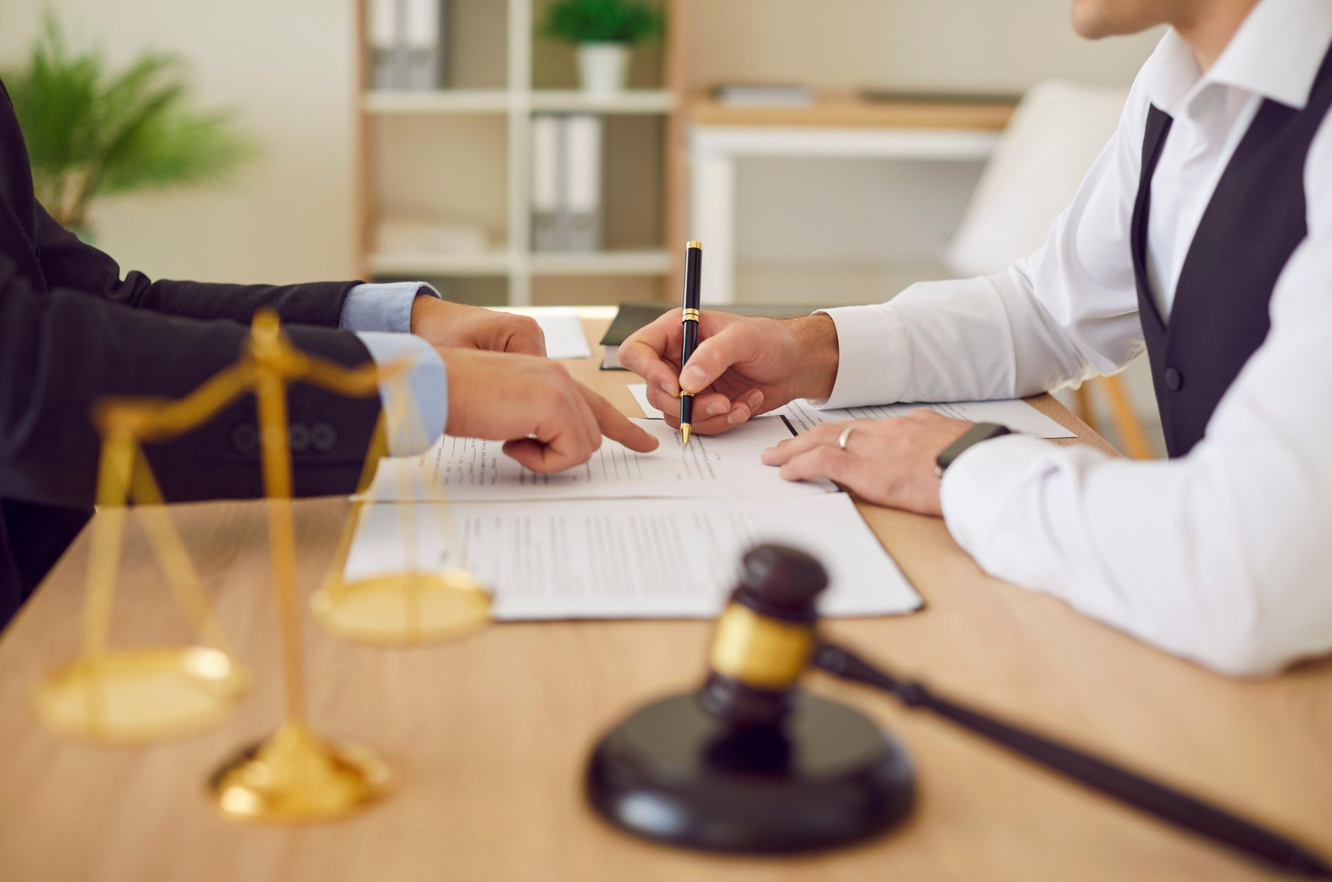 Lawyers signing a contract at a desk with scales of justice and a gavel nearby