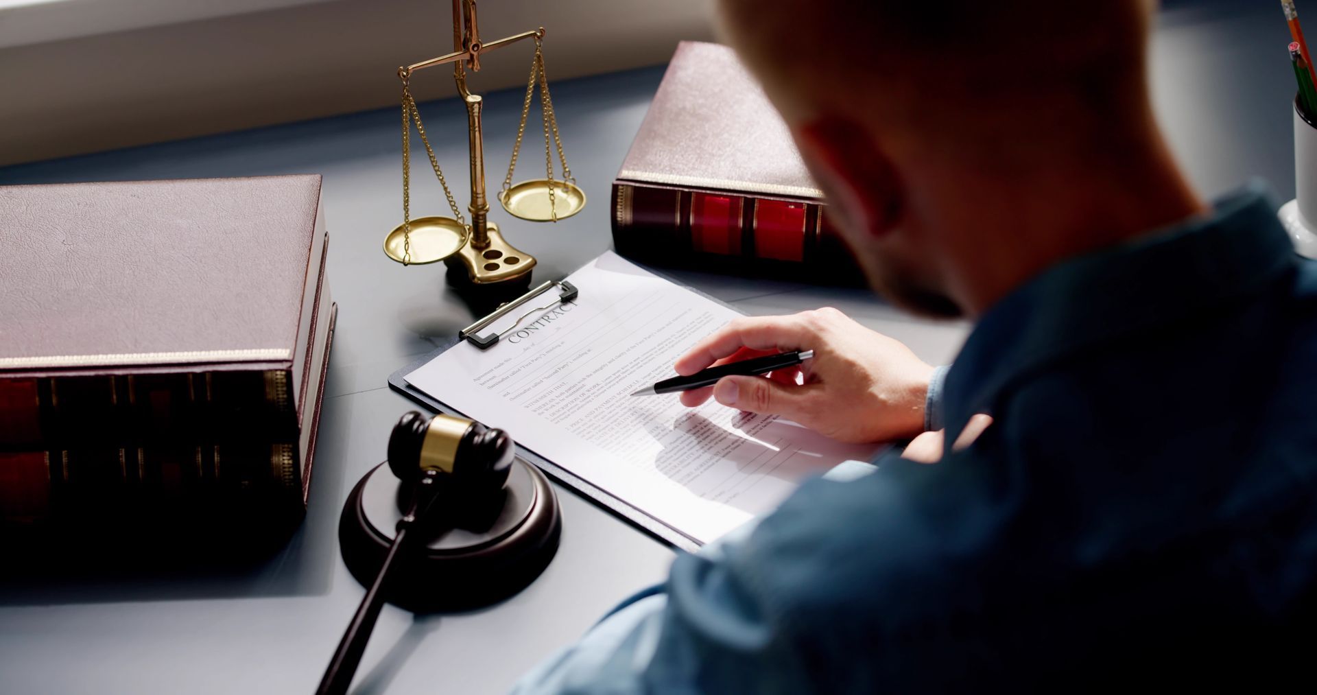 Lawyer writing notes beside scales of justice and a gavel on a desk