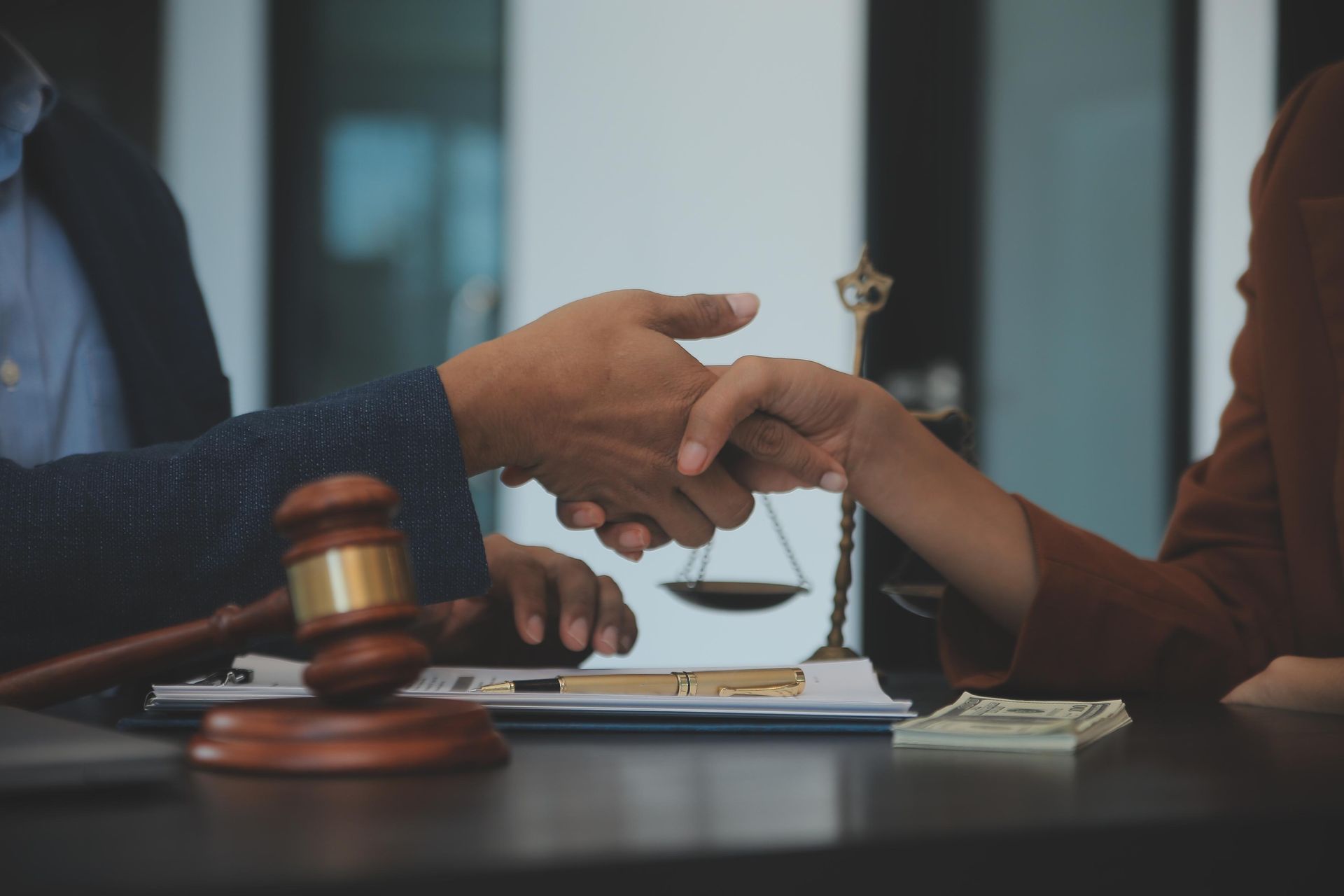 Two hands exchanging a document beside a judge’s gavel in a courtroom-like setting