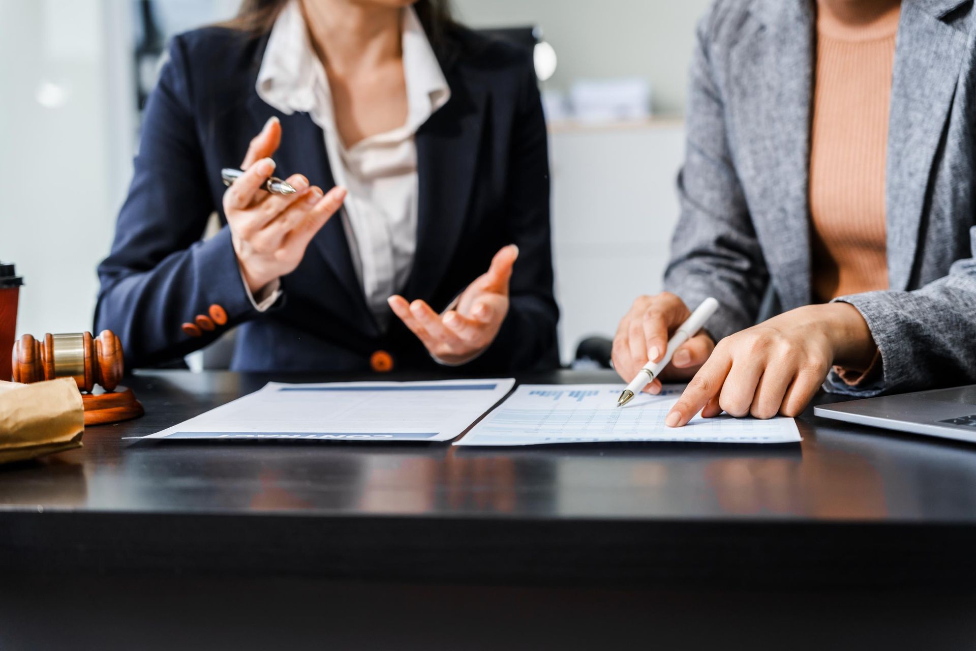 Two people in business attire discussing documents at a conference table, one holding a pen and gesturing.