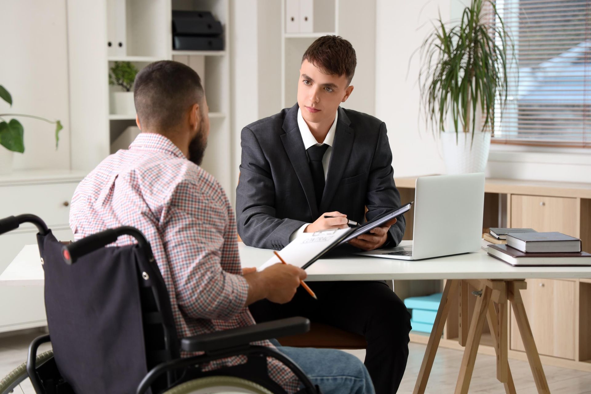 Office meeting with a man in a suit discussing documents with a wheelchair user at a desk