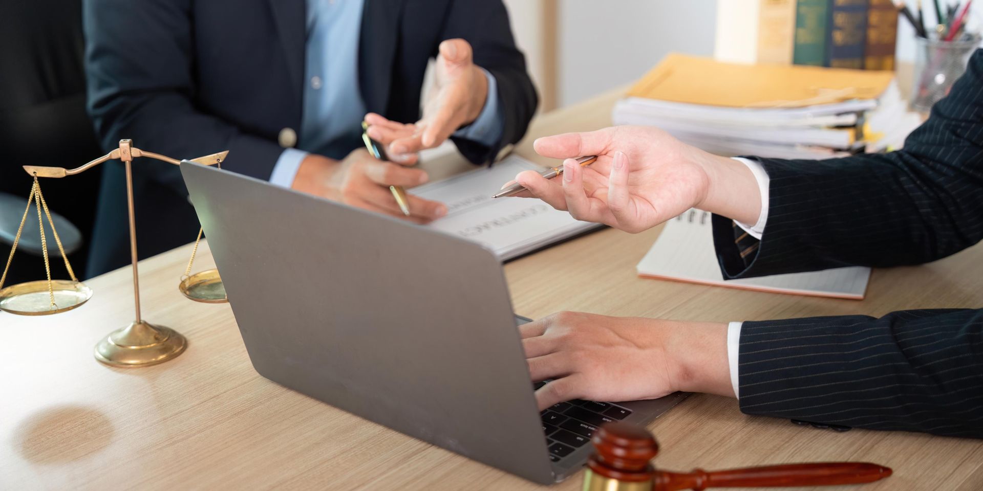 Hands using a laptop during a meeting beside a gold scales of justice statue
