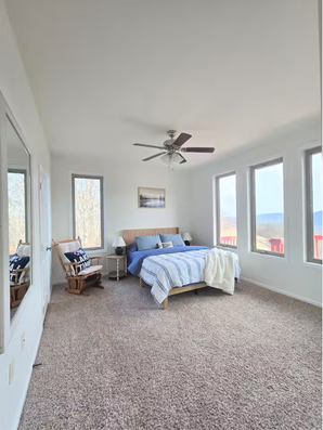 Bedroom with blue bed, rocking chair, and large windows.