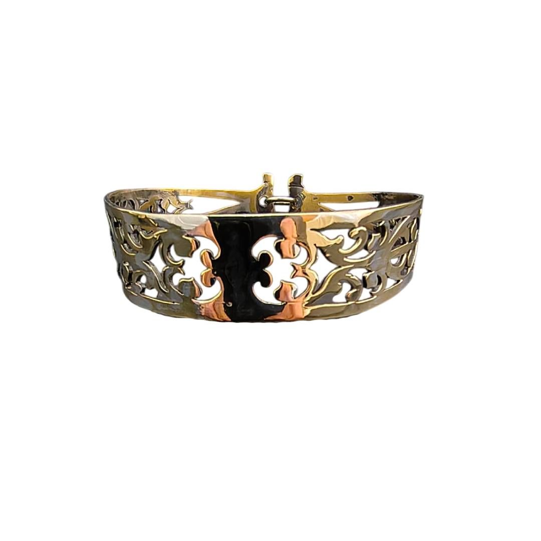 Pulsera ornamentada de oro y plata con diseño floral calado sobre fondo blanco.