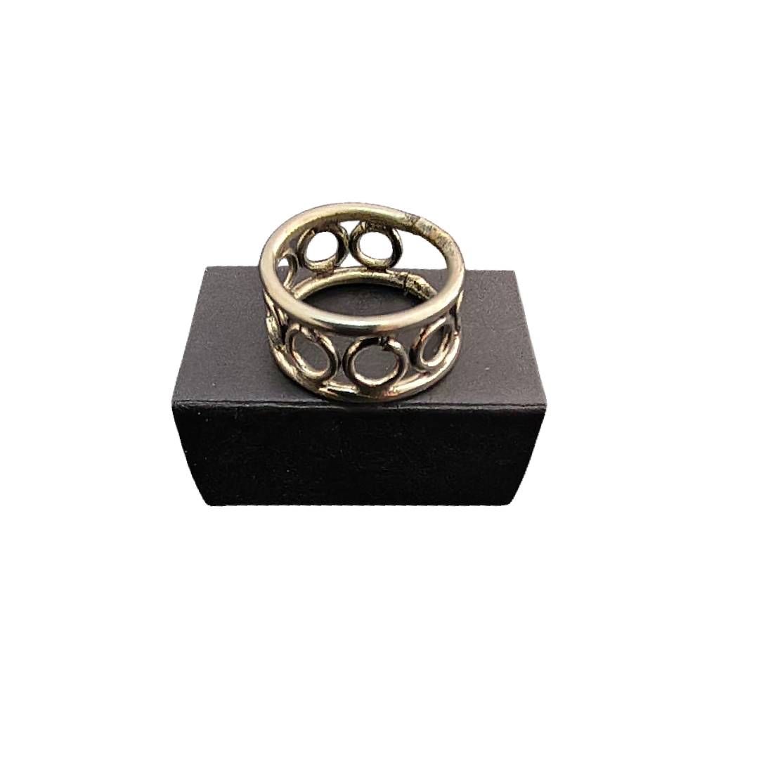 Anillo de oro con un patrón circular calado, exhibido sobre un pedestal negro sobre un fondo blanco.