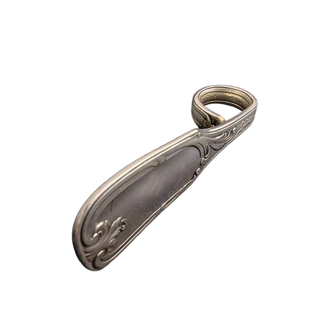 Colgante de cuchara de plata con argolla en forma de lazo sobre fondo blanco.