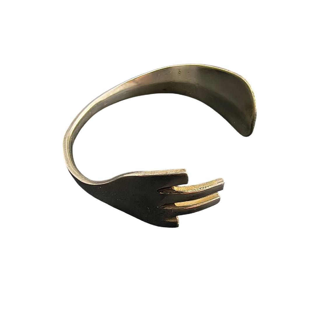 Brazalete metálico curvado con abertura y tres puntas doradas.