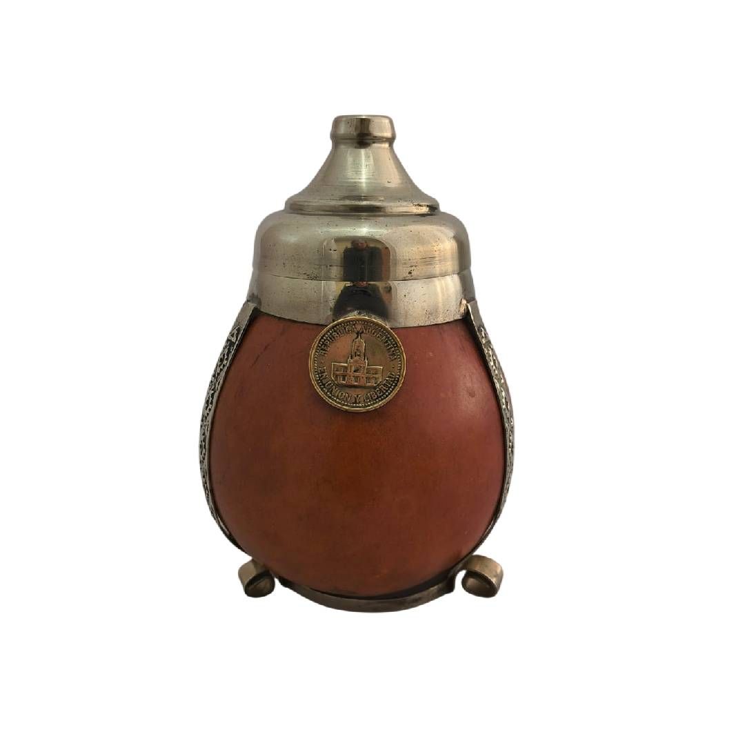 Objeto antiguo de metal de cobre y plata con cuerpo de color marrón rojizo y un emblema de medallón colgante.