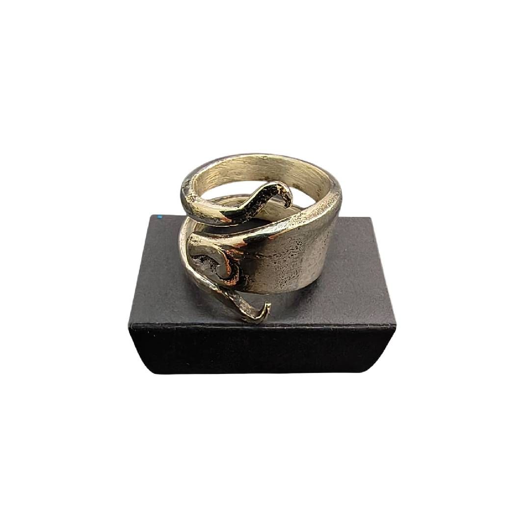 Anillo retorcido de oro sobre un soporte de exhibición negro, centrado sobre un fondo blanco.