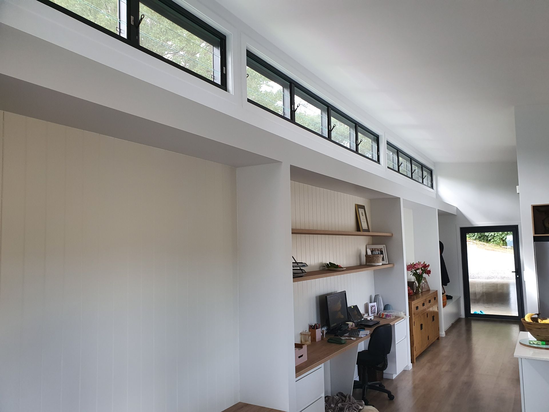 A living room with a desk , chair , shelves and windows.