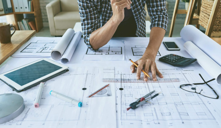 A man is sitting at a table working on a blueprint.
