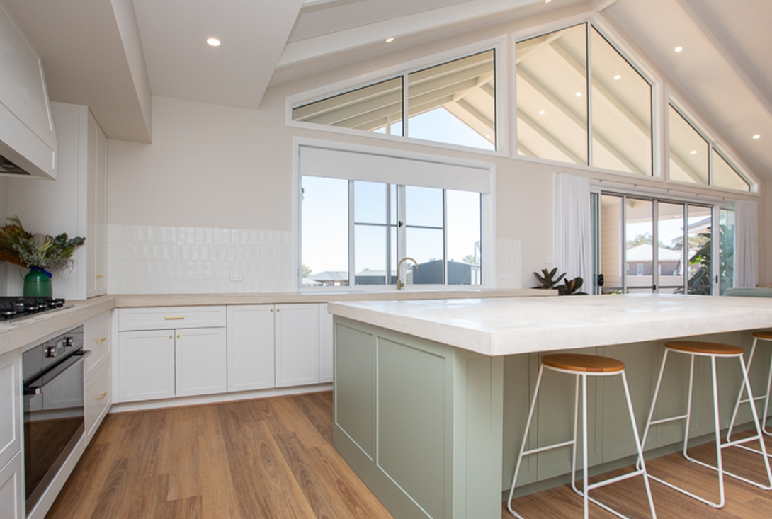 A kitchen with a large island and stools and a vaulted ceiling.