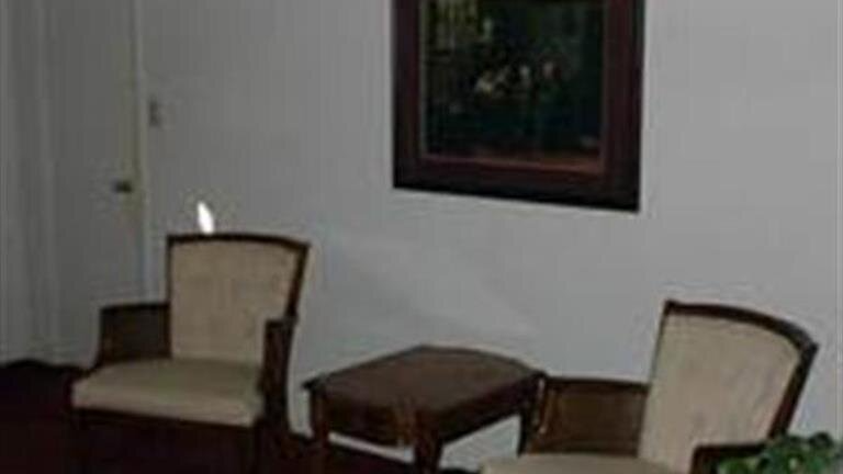 Two beige armchairs and a small wooden table in a dimly lit room beneath a framed picture