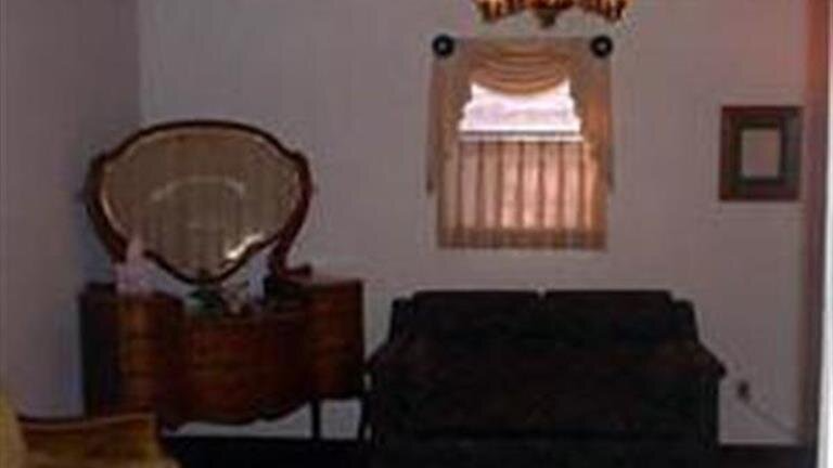 Dim living room with a dark couch, wooden dresser, ornate mirror, and a window with striped curtains.