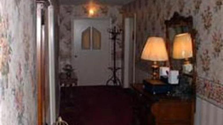 Narrow floral hallway with a dark runner, lamps on a table, and double doors at the far end
