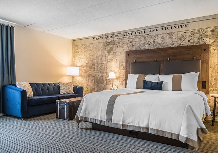 Hotel room with king bed, blue sofa, floor lamp, and rustic stone accent wall