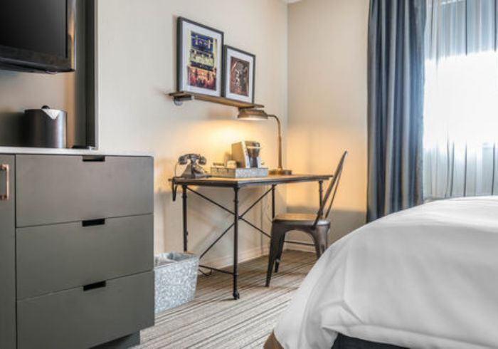 Modern hotel room with a bed, desk, chair, dresser, and window with curtains