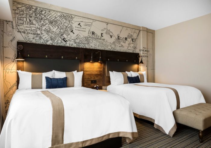 Hotel room with two neatly made twin beds, dark wood headboard, and beige patterned wall art