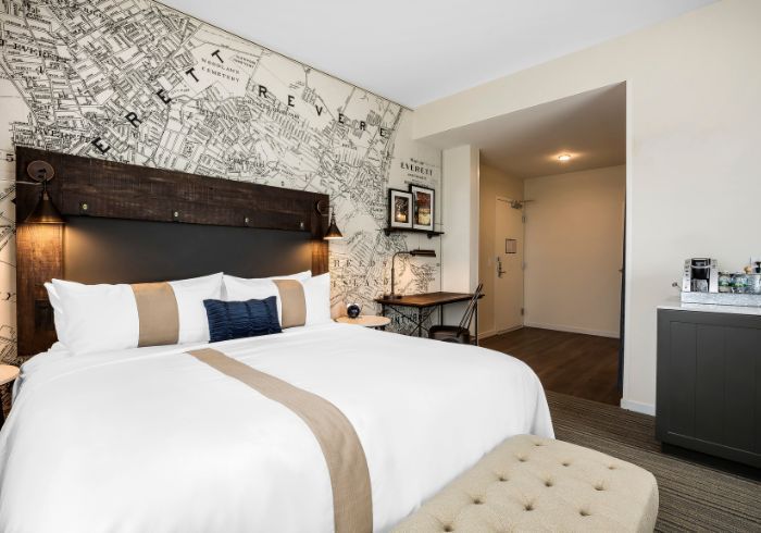Modern hotel room with a large white bed, map-patterned wall, and hallway view