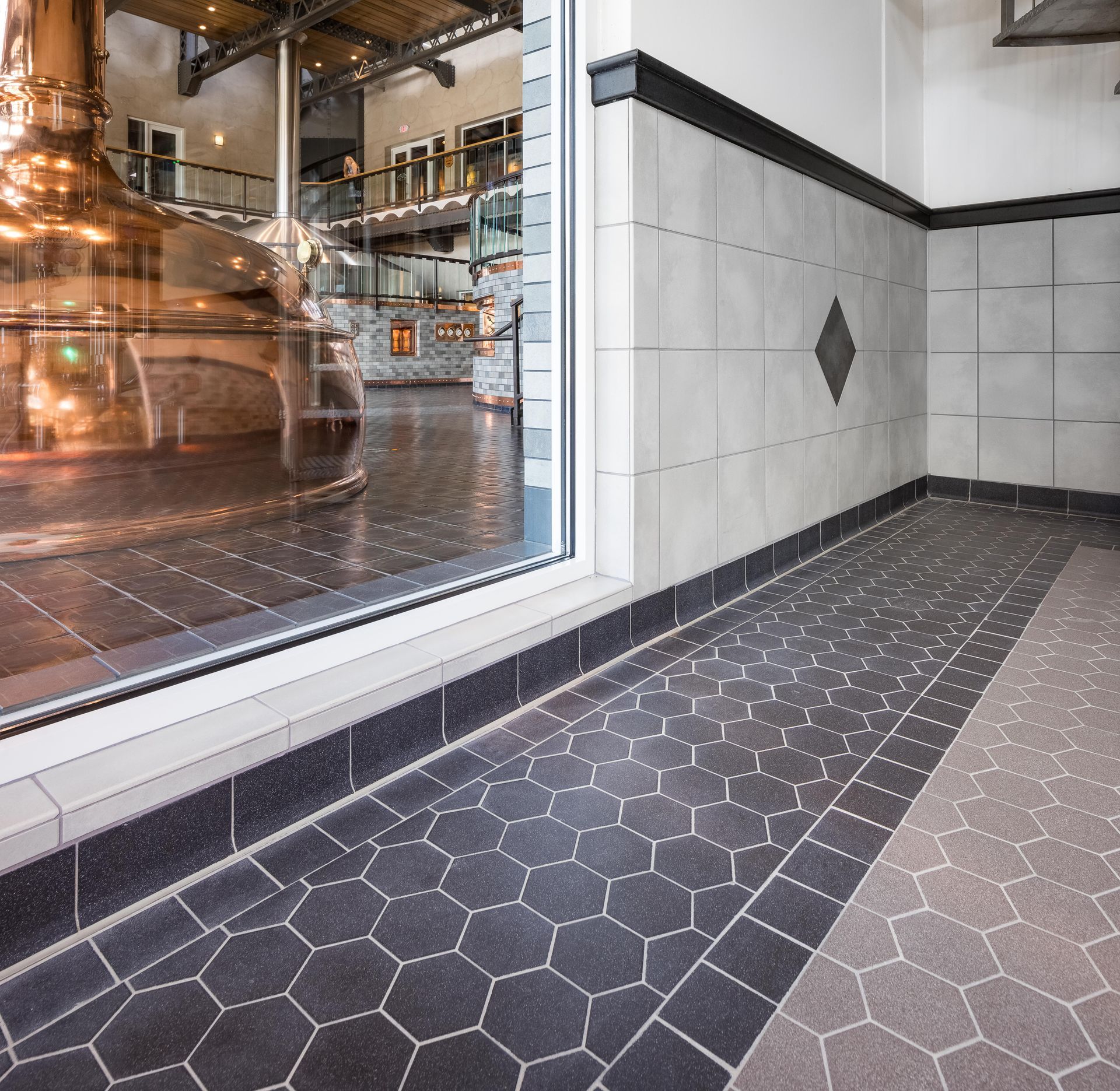 Tiled interior with a large window overlooking a brewery’s copper tanks and industrial equipment