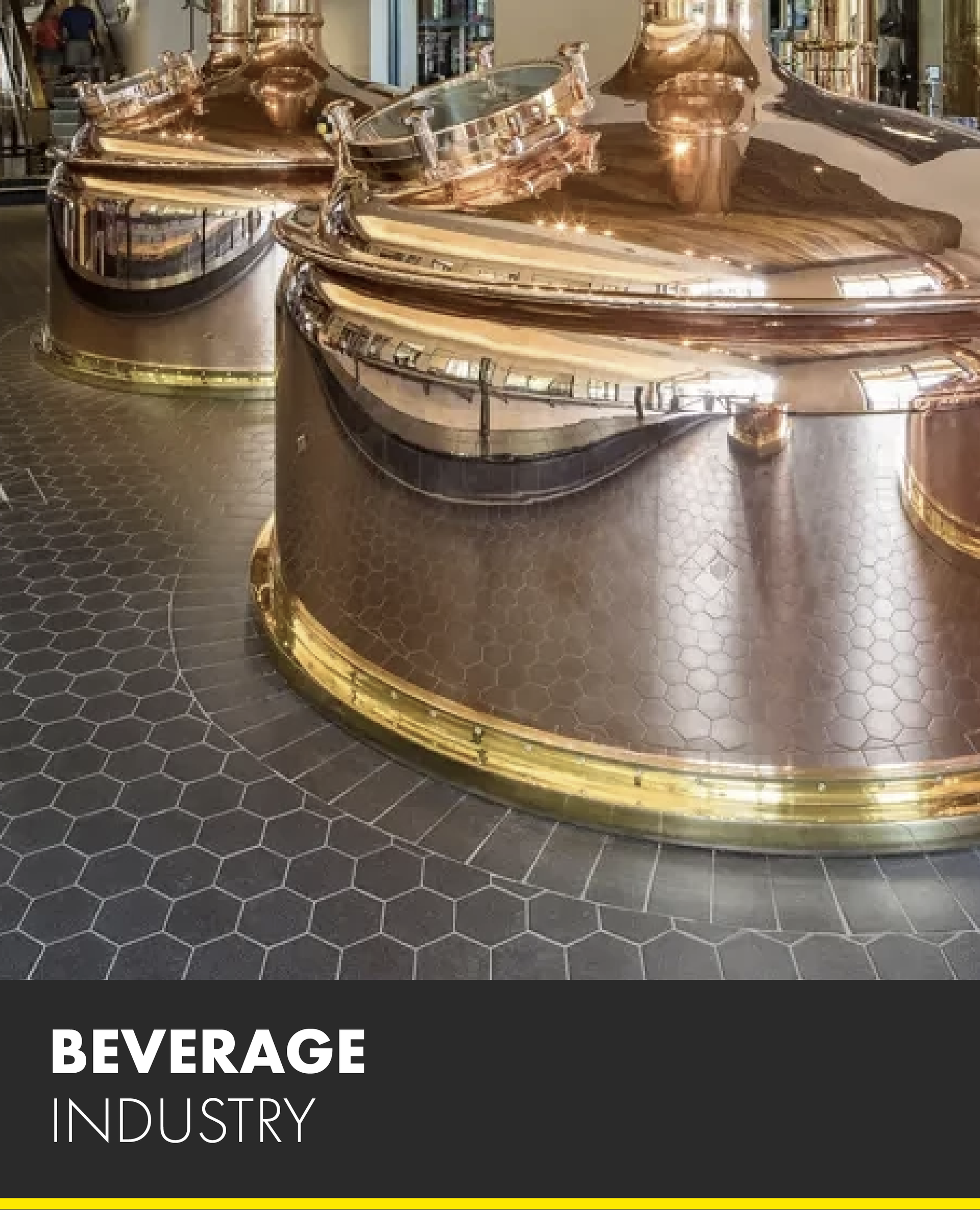 Two large copper pots are sitting on a tiled floor in a beverage industry.
