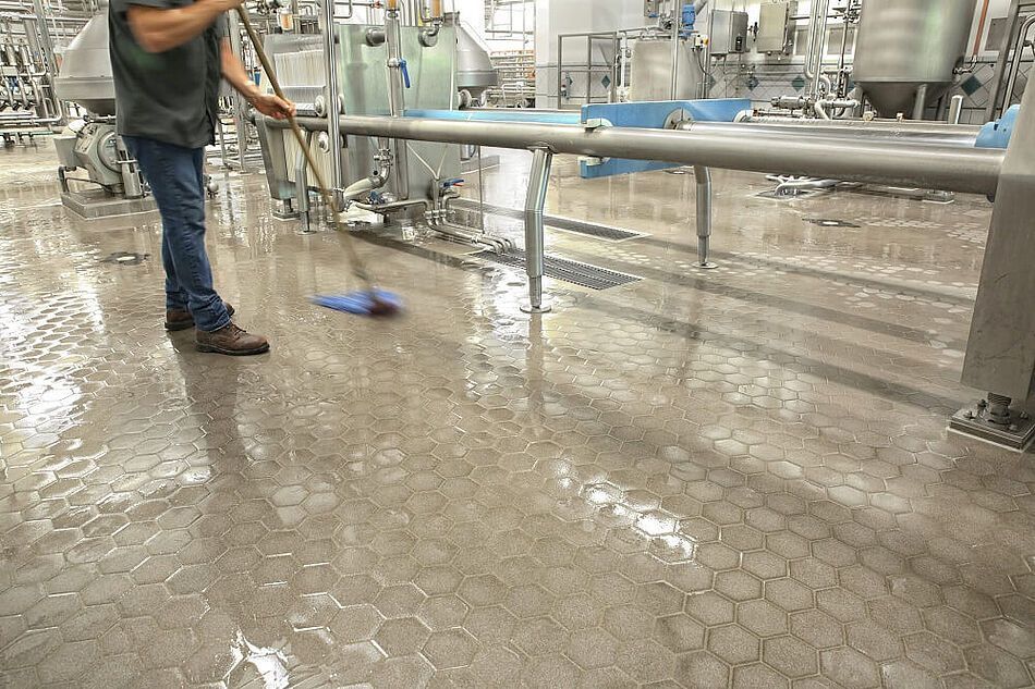 Worker mopping a wet industrial factory floor beside stainless steel equipment
