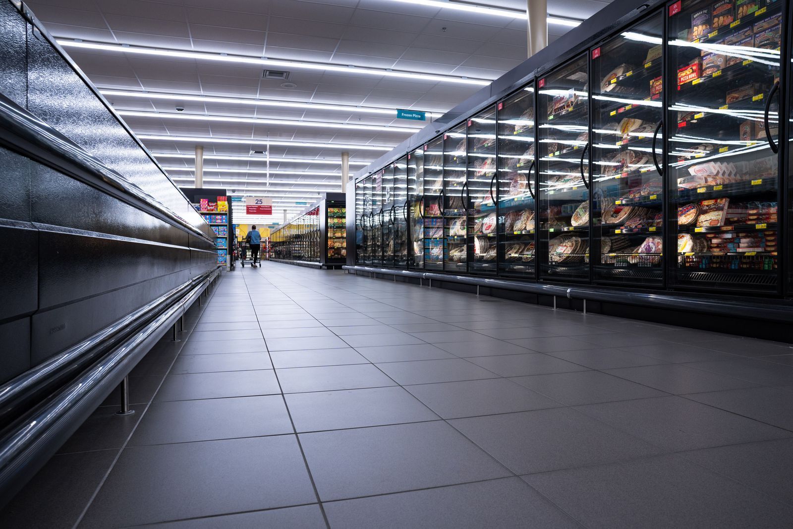 Empty grocery store aisle with tiled floor, bright overhead lights, and glass freezer cases on the right.