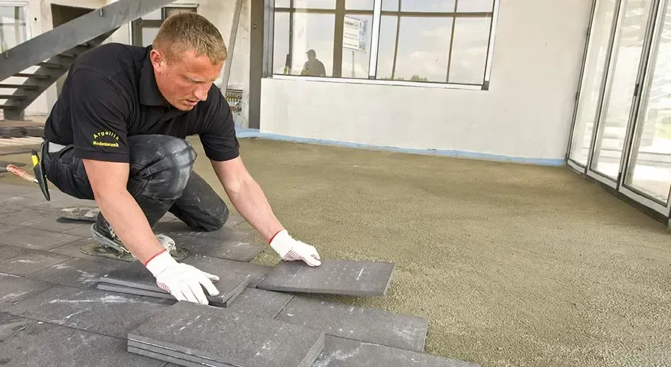 A man is kneeling down installing tile