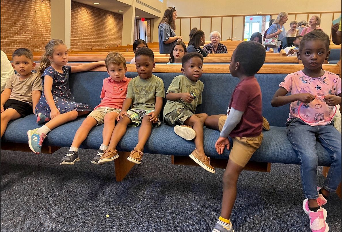 A group of children are sitting on a bench in a church.