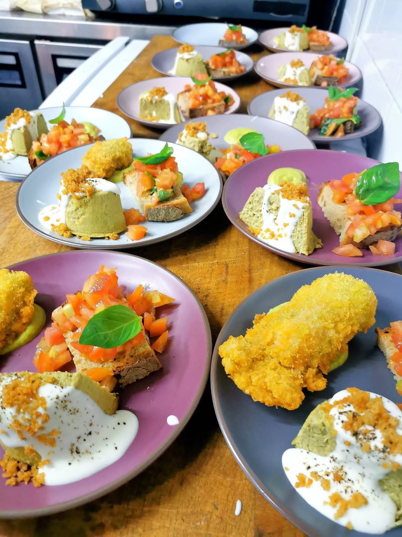 Piatti gourmet assortiti disposti su un tavolo di legno, con guarnizioni e salse colorate.