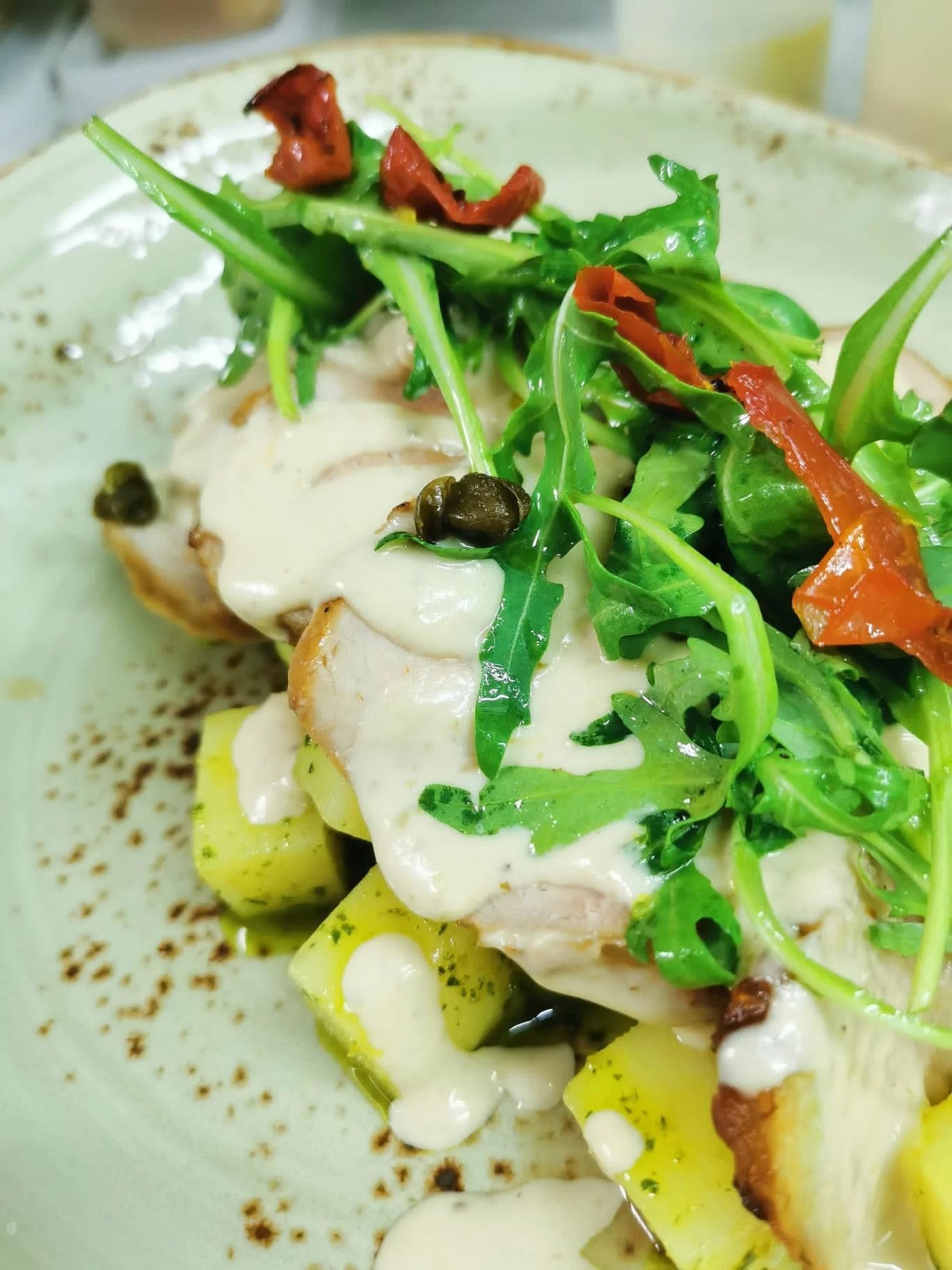 Piatto gourmet impiattato con salsa bianca, guarnizione verde e strisce di peperone rosso su un piatto bianco.