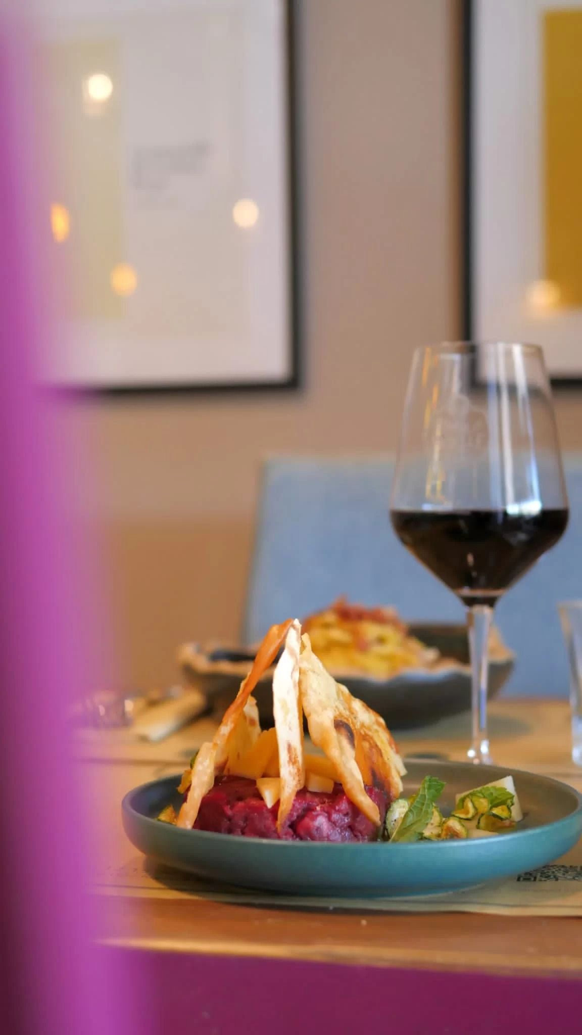 Un calice di vino accanto a un dessert gourmet impiattato in un ristorante illuminato da luci soffuse.