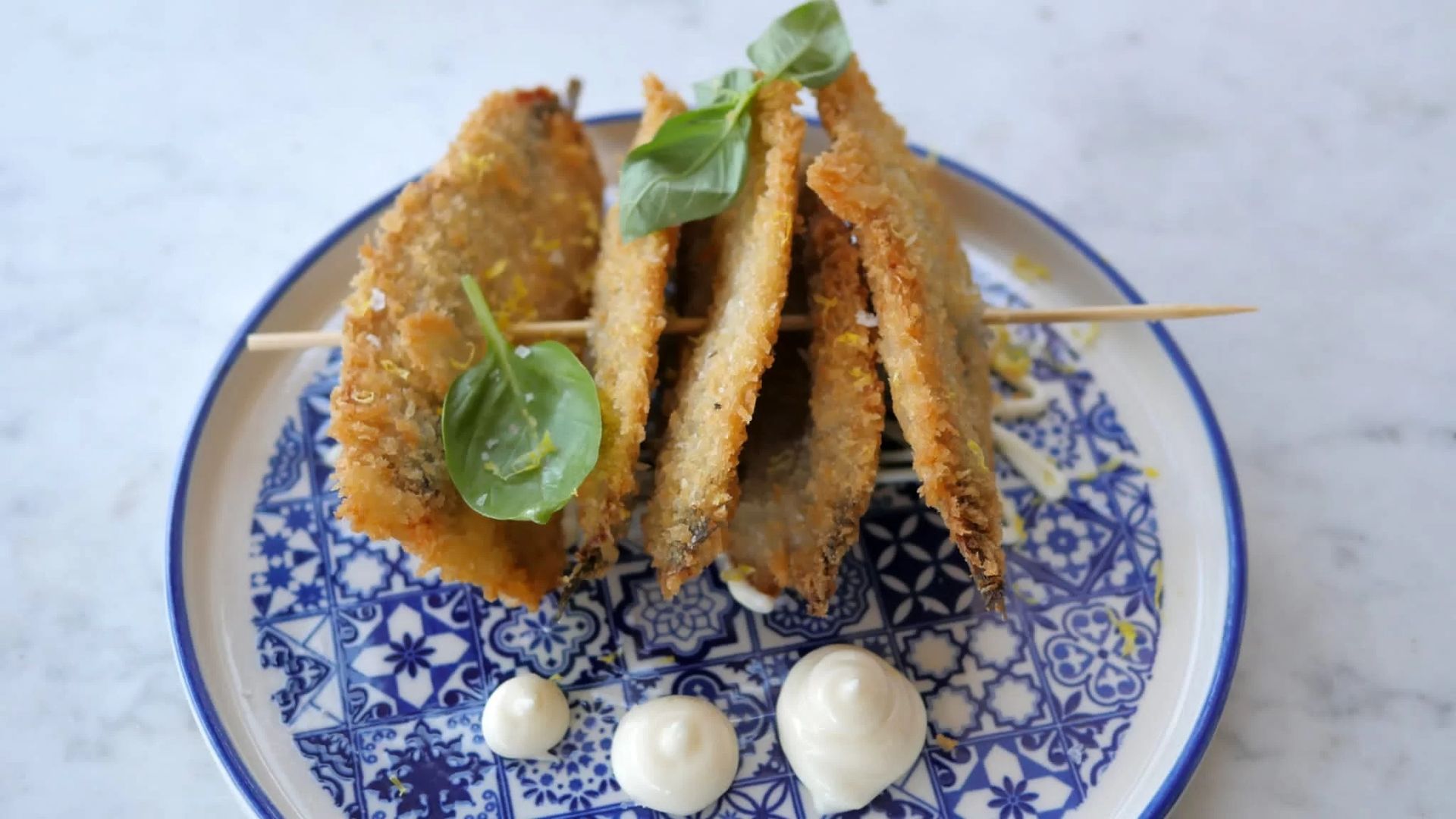Frittelle triangolari servite su un piatto decorato in bianco e blu, con ciuffi di salsa bianca ed erbe aromatiche.