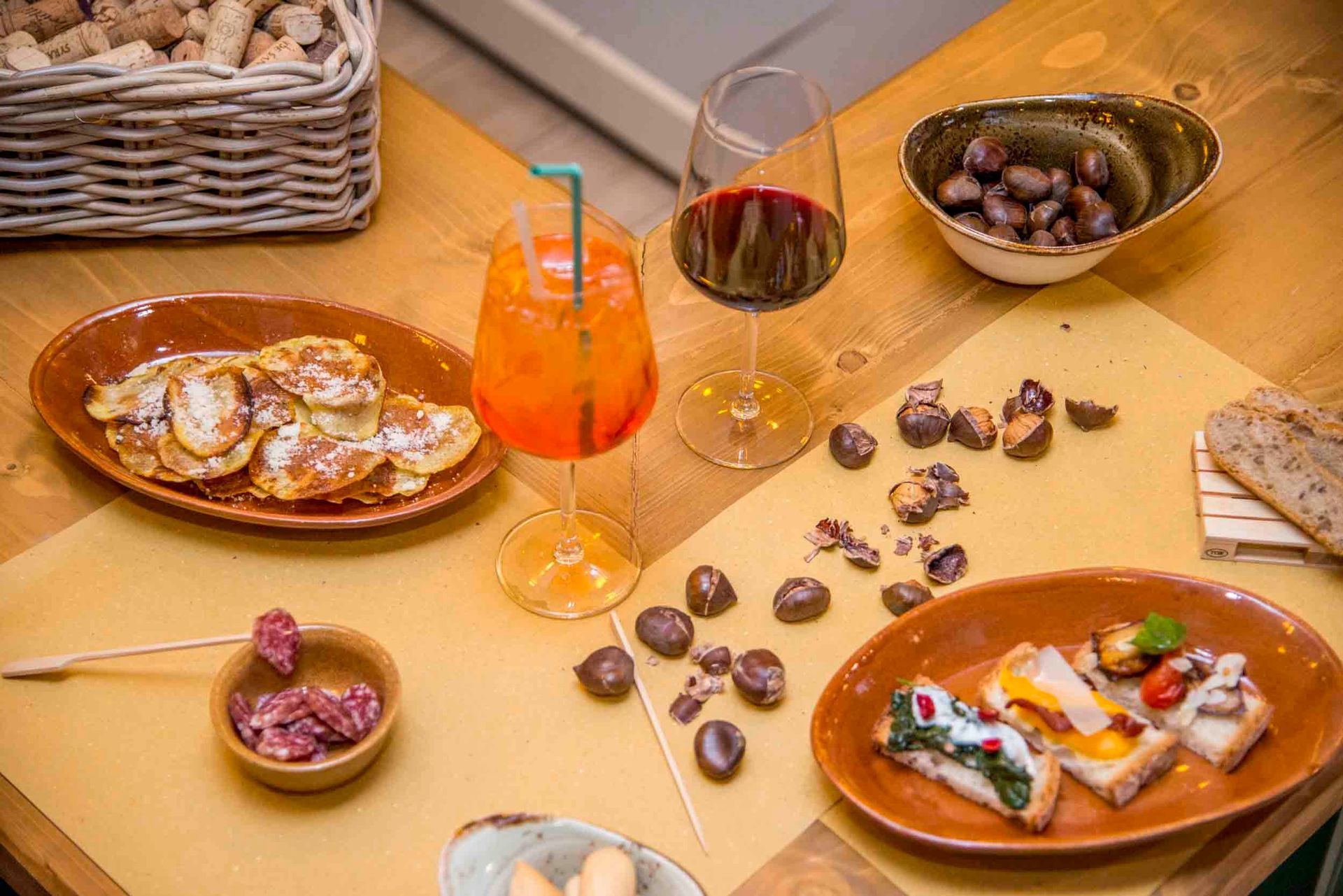 Tavolo con tapas, cocktail all'arancia, bicchieri da vino e olive sparse su una superficie di legno.