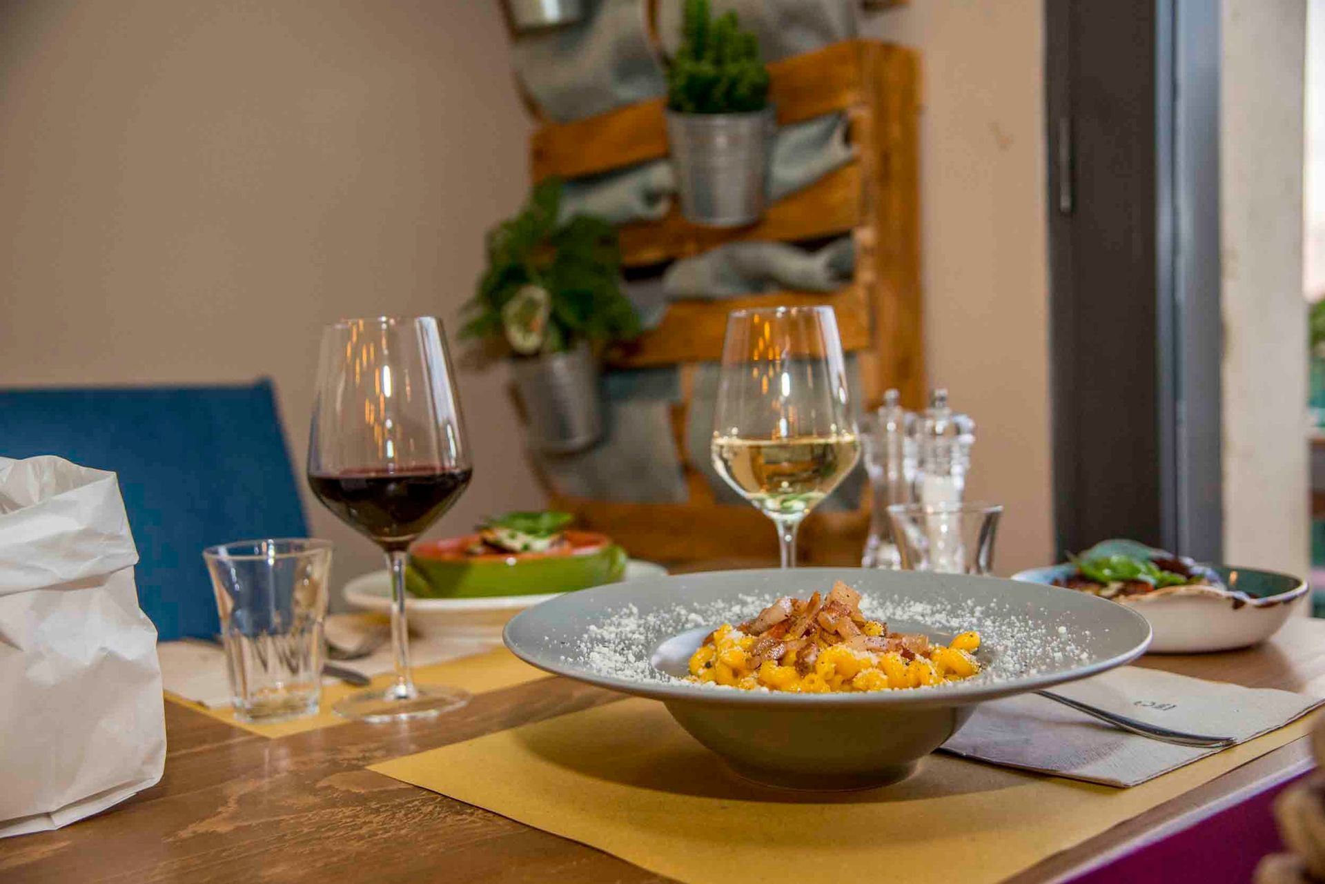 Tavolo da pranzo apparecchiato per un pasto con bicchieri da vino, pietanze servite e un piatto di pasta in un'accogliente atmosfera da ristorante.