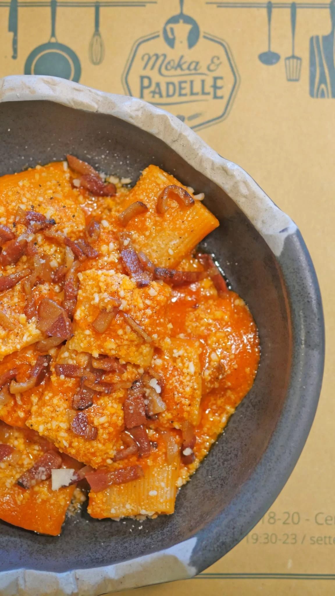 Piatto di pasta al sugo di pomodoro con formaggio grattugiato su tovaglietta di carta marrone