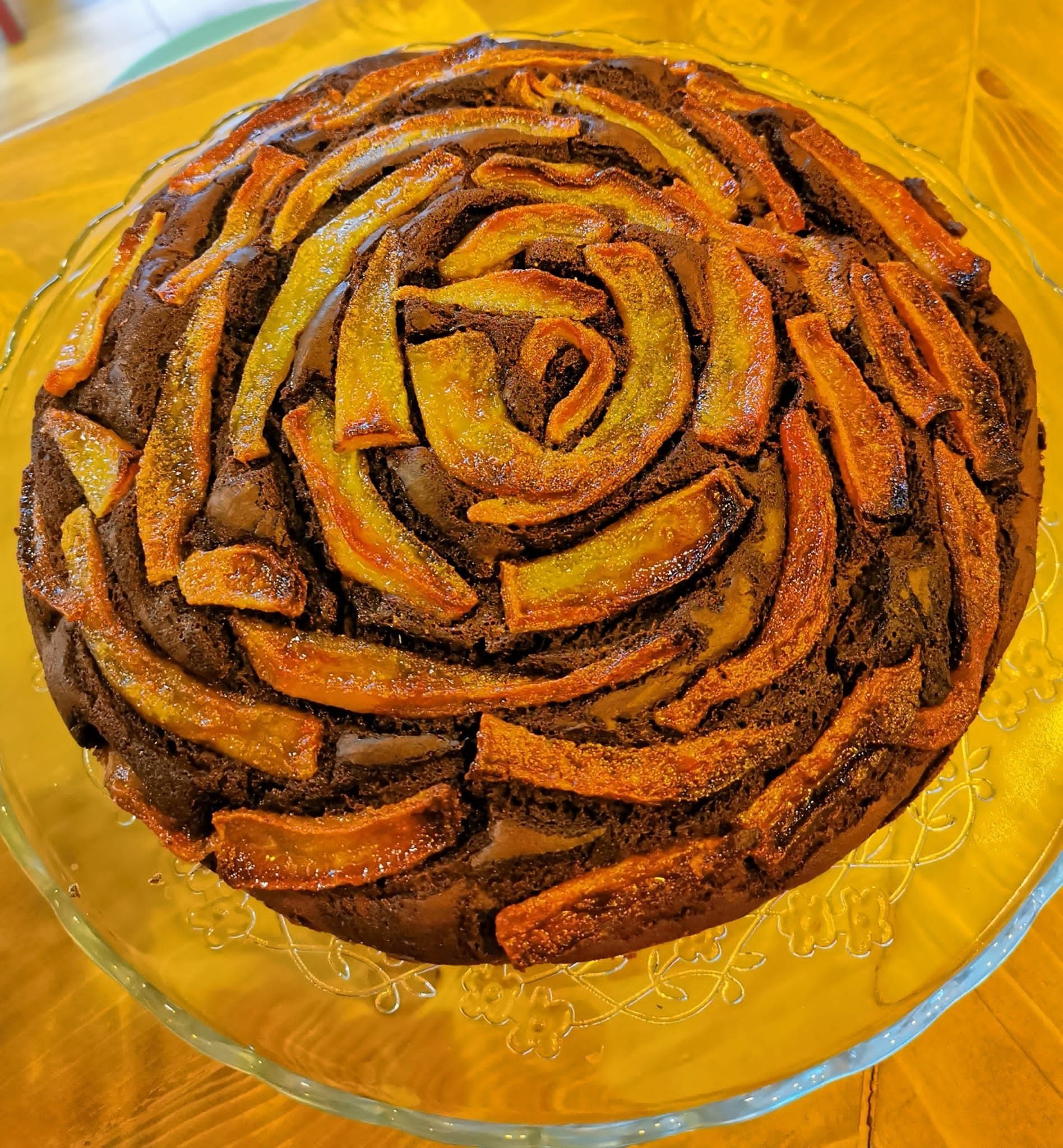 Crostata di frutta a forma di rosa su un piatto di vetro con una guarnizione a spirale caramellata.