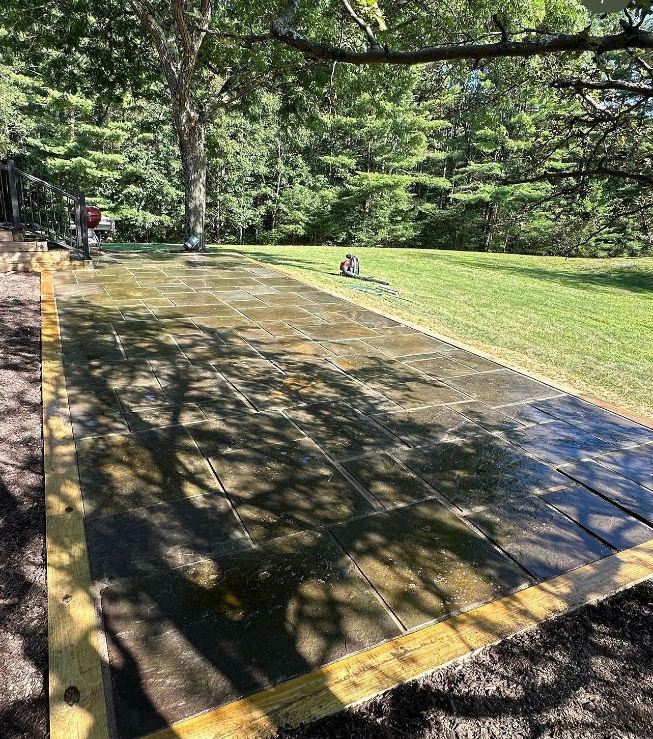 A wet wooden deck framed with yellow boards sits outdoors. A person is visible in the background.
