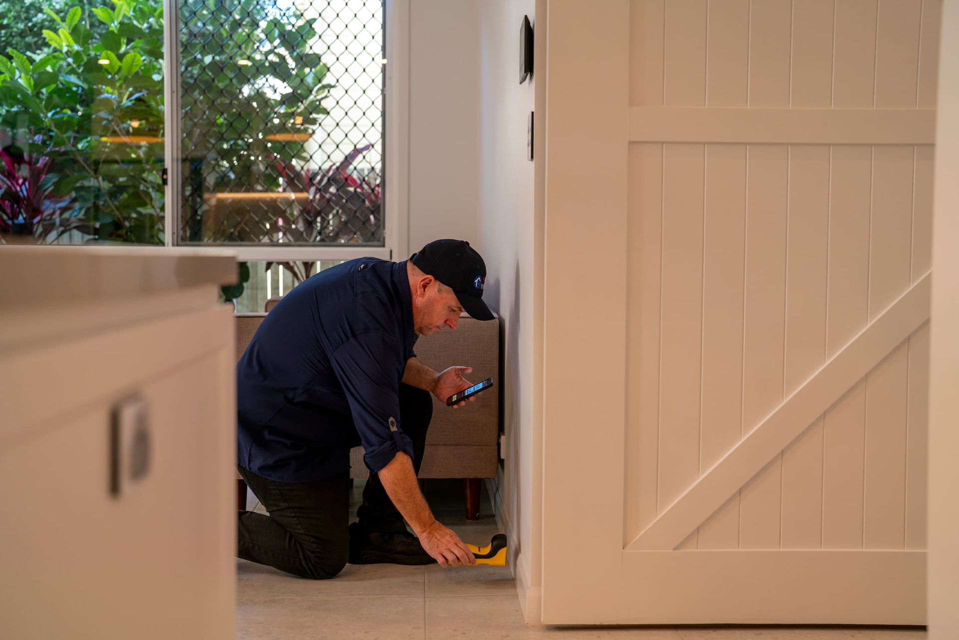 Worker Using a Tool Near the Floor in a Bright Indoor Entryway — National Pest Solutions in Upper Caboolture, QLD